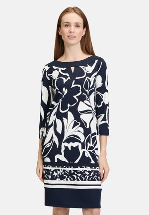 Marineblaues Kleid mit weißem Blumenmuster, Dreiviertelärmeln, weitem Ausschnitt und Schlitzdetail vorne; glatte Stoffstruktur.