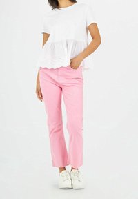 Haut peplum en coton blanc avec des finitions en œillets festonnés assorti à un pantalon en coton rose clair et des baskets blanches, présentant une taille ajustée et une coupe décontractée.