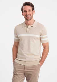 Beige kortärmad polo-shirt med ribbad krage, tre-knappsknäppning och vita ränder på ärmarna. Slät stickad textur.