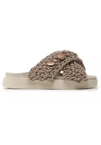 Beige vävd slide sandal med en texturerad vävd ovandel och dekorerande stenar på remmen, placerad på en ljus tonad, dämpad sula.