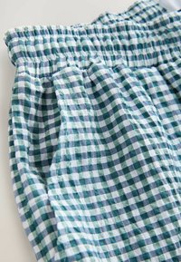 Blauw-groen geruit stof met een zachte textuur, voorzien van een elastische tailleband en geplooide details. Het materiaal lijkt lichtgewicht en ademend.