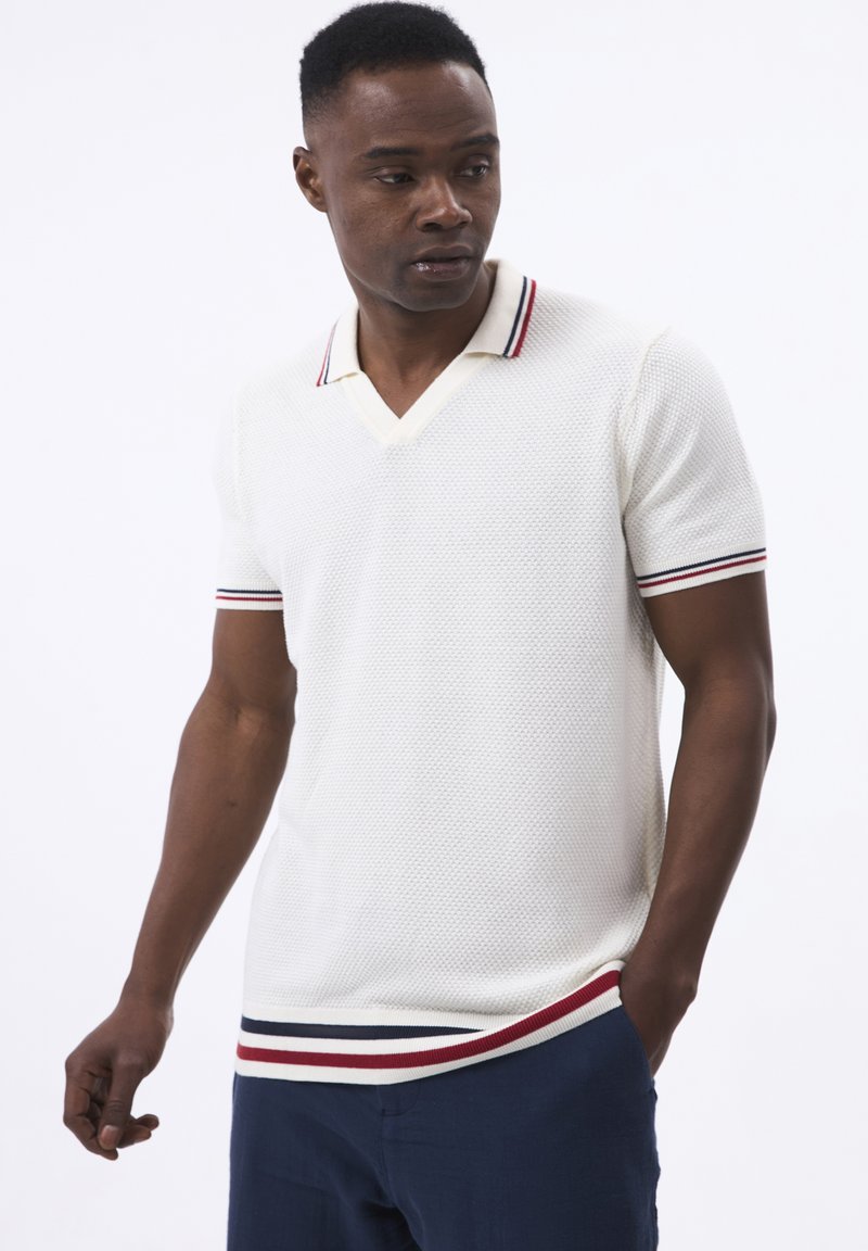 Polo de cuello en V en color crema con tejido texturizado, mangas cortas y ribetes a rayas rojos y marinos en el collar y el dobladillo.