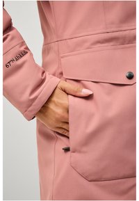 Roze waterdichte jas met een ritszak, knoopdetail en geborduurd merkvignet op de mouw. Glad, lichtgewicht stof.