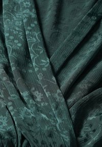 Ciemnozielona tkanina z kwiatowym wzorem. Faktura z marszczeniami i warstwowe drapowania tworzące głębię i ruch.