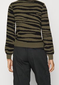 Olivgrüner Pullover mit schwarzen Zebra-Streifen, gerippten Bündchen und Saum, weichem Material mit Struktur, Rundhalsausschnitt und schmaler Passform.
