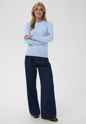 Maglione lavorato a maglia di un blu chiaro con scollo rotondo e polsini a coste, abbinato a jeans scuri a gamba larga e scarpe marroni.