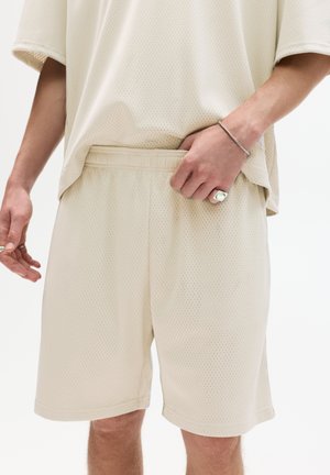 Ensemble de sport en maille beige clair, composé d'un haut ample à manches courtes et d'un short. Taille élastique notable et tissu texturé et respirant.