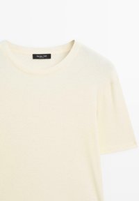 Krémové tričko vyrobené z měkké, hladké bavlny. Má klasický kulatý výstřih a krátké rukávy, bez vzorů nebo akcentů.