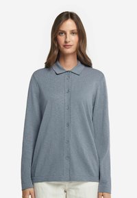 Långärmad skjorta med knappar i mjukt blått tyg, med krage, hel knäppning fram och en avslappnad silhuett. Diskret ribbad textur.
