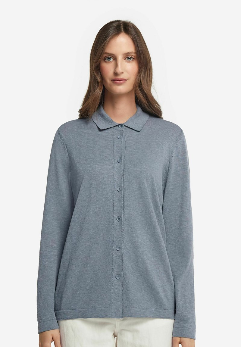 Långärmad skjorta med knappar i mjukt blått tyg, med krage, hel knäppning fram och en avslappnad silhuett. Diskret ribbad textur.
