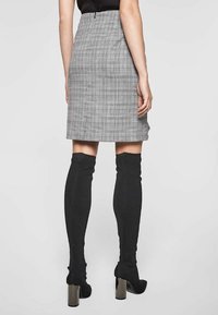 Grå rutigt kjol med en åtsittande design som når över knäet. Bärs med svarta knähöga strumpor och klackade ankelkängor.