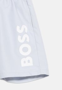 Ανοιχτό γκρι σορτς με λευκή επιγραφή "BOSS" τυπωμένη κάθετα κοντά στο τελείωμα και πλαϊνή τσέπη με ορατή ραφή.