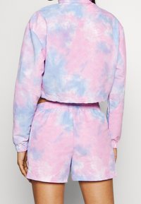 Zestaw składający się z krótko przyciętej kurtki tie-dye i szortów w pastelowych odcieniach różu i niebieskiego. Miękka tkanina z elastyczną talią i mankietami.