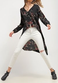 Černý dlouhý rukáv top s květinovým vzorem, vrstvený design a výstřih do V. Kombinováno s bílými roztrhanými skinny džínami a černými kotníkovými botami.