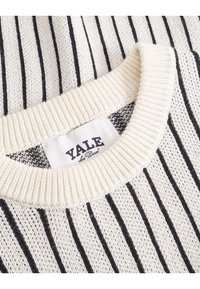 Klassisk bomullsgenser med vertikale svarte striper på en kremfarget bakgrunn, med ribbestrikket halslinning og et «Yale»-merke.