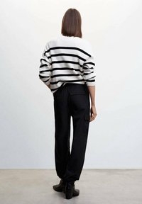 Sweater rayé noir et blanc avec une texture côtelée, associé à un pantalon cargo noir avec des poches latérales et une coupe décontractée. Bottines noires.