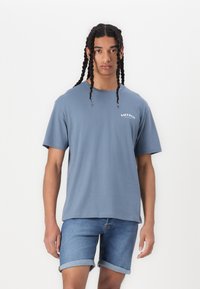 Blå bomull t-skjorte med korte ermer, rund hals og tekstdetalj på fronten; kombinert med denimshorts med oppbrettede ermer.
