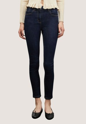 Jeans ajustados de color azul oscuro con una textura suave, diseño de cinco bolsillos y detalles de costura sutiles, combinados con bailarinas negras.
