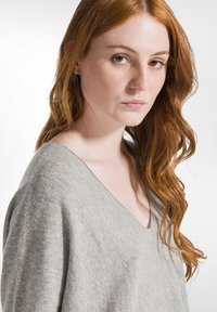 Hellgrauer, gestrickter Pullover mit tiefem V-Ausschnitt und lockerer Passform, der eine weiche Textur und zarte Farbschattierungen zeigt.