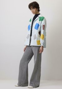 Svijetloplavi preveliki sako s višečepiranim zakrpama u zelenoj, žutoj, plavoj, smeđoj i sivoj boji; uparen s sivim širokim trapericama i bijelim cipelama.