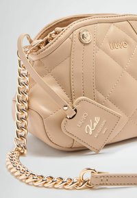 Beige gesteppte Leder-Handtasche mit goldenen Beschlägen, ausgestattet mit einem Kettenriemen und einem Markenanhänger, der "Kate Re-Edition 2012" vermerkt.