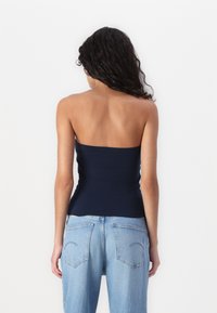 Marineblå strapless topp med en tettsittende design, sammen med lyseblå høy midje jeans som har baklommer og en klassisk denim tekstur.