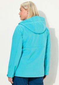 Turkosa softshell-jacka med huva, som har en mjuk textur, elastiska ärmar och en söm tvärs över ryggen. Praktisk design för utomhusbruk.