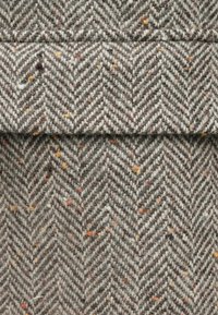 Μάλλινο ύφασμα σε σχέδιο ψαροκόκαλο με γκρι και μπεζ χρώμα, έχοντας πολύχρωμα στίγματα παντού και ευχάριστη, υφασμάτινη υφή.