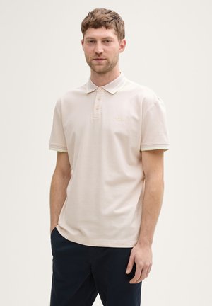 Lichtroze polo shirt met een zachte textuur, voorzien van een kraag met een contrasterende groene bies en een subtiel logo op de borst.
