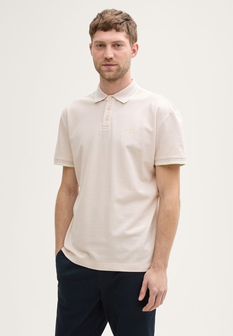 Helles rosa Poloshirt mit weicher Textur, einem Kragen mit kontrastierendem grünen Besatz und einem dezenten Logo auf der Brust.