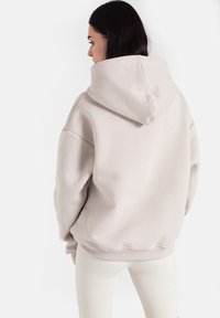 Jasnoszara, oversize bluza z kapturem o miękkiej strukturze, z dużym kapturem i ściągaczami, zestawiona z białymi legginsami z prążkowanej tkaniny.