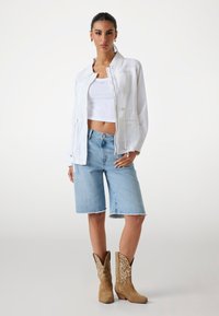 Biała, lekka kurtka z kołnierzykiem, noszona na białej bluzce typu crop top i niebieskich szortach dżinsowych. Beżowe kowbojki z dekoracyjnym przeszyciem.