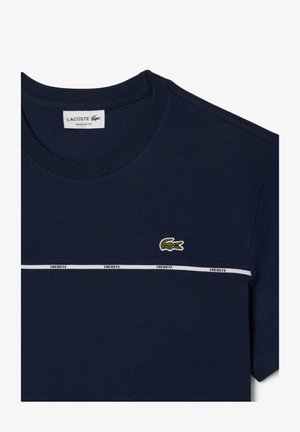 Σκούρο μπλε βαμβακερό t-shirt με στρογγυλή λαιμόκοψη, με άσπρη ρίγα και το λογότυπο "LACOSTE", καθώς και ένα μικρό πράσινο κροκοδειλάκι στο στήθος.