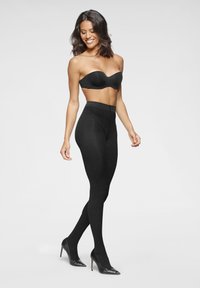 Schwarze Leggings aus dehnbarem Material, mit hohem Bund und figurbetontem Schnitt, kombiniert mit schwarzen Stilettos.