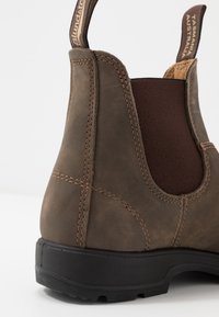 Bottine en cuir marron avec semelle noire, panneau latéral élastique et languettes en tissu étiquetées "Blundstone" et "Tasmania Australia".