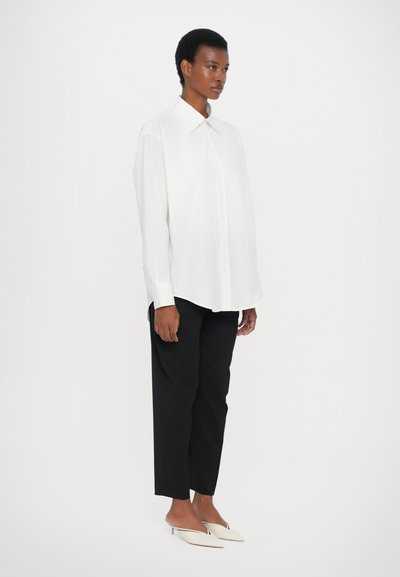 White button-up shirt with a large collar, paired with black tapered pants and white pointed-toe mules. Smooth fabric, minimalistic design.
