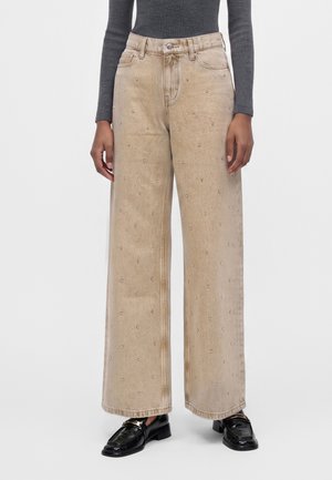 Beige vidde jeans med små nitter, båret med en mørkegrå ribbet langærmet top og sorte loafers.