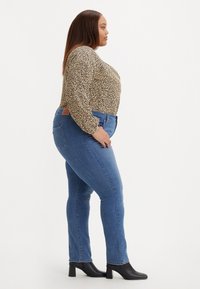 Jeans skinny blu con un lavaggio medio e tasche frontali, abbinati a un top a maniche lunghe con stampa leopardata e stivaletti neri con tacco.