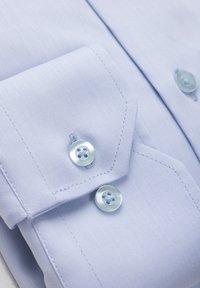 Hele sinise kleitpaiga mansett kahe ümmarguse, läbipaistva nööbiga ja detailse õmblusega sileda kangaga.