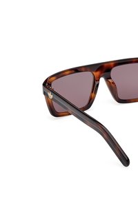 Ochelari de soare cu tortoiseshell, lentile maro, rame unghiulare și un accent de logo auriu pe lateral. Material plastic neted cu un design elegant.
