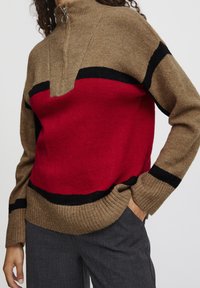 Strickpullover mit hohem Kragen, braunem Körper und rotem Mittelteil sowie schwarzen Streifen an den Schultern und Ärmelbündchen. Gerippter Saum.