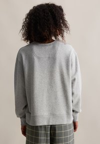 Grauer Sweatshirt mit lockerer Passform, geripptem Rundhalsausschnitt und Oversized-Schultern. Sanfte Textur mit sichtbaren Nähten an den Säumen.