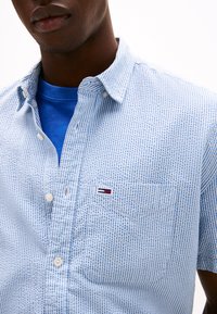 Modrobílé pruhované tričko s krátkými rukávy a límečkem na knoflíky, s náprsní kapsou a malou logo nášivkou. Texturovaná látka.