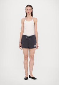 Bieli tank top v kombinácii s tmavosivými šortkami s elastickým pásom a šnúrkou na sťahovanie. Na prednej strane šortiek je vytlačené logo.