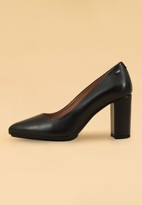 Scarpa décolleté nera in pelle con tacco alto, punta affusolata, superficie liscia e tacco a blocco per stabilità, caratterizzata da un sottile dettaglio del logo sul tacco.