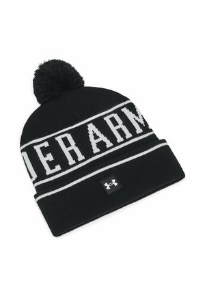 Juodas megztas kepurė su balta užrašu "UNDER ARMOUR", su pom-pomu viršuje ir mažą juodą logotipo etikete ant krašto.