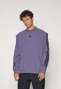 Sweatshirt viola con strisce nere sulle maniche, colletto a coste e logo sul petto. Tessuto morbido, vestibilità rilassata, design moderno.