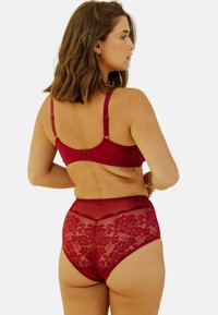 Ensemble de lingerie rouge comprenant un soutien-gorge lisse avec des bretelles réglables et une culotte en dentelle taille haute avec des motifs floraux et des panneaux transparents.