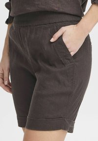 Dark brown linen shorts with an elastic waistband, side pockets, and cuffed hems, featuring a soft texture and relaxed design.