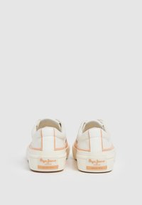 Zapatillas de lona blancas con suaves acentos melocotón, suelas de goma planas y detalle del logo en el talón, con costuras decorativas y un diseño de corte bajo.